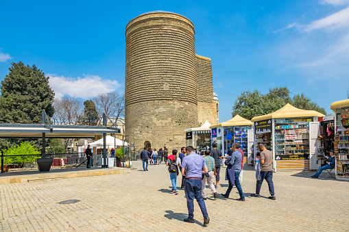 People walk beside the landmark Maiden Tower, a UNESCO World Heritage Site in Baku Azerbaijan, on a sunny day.