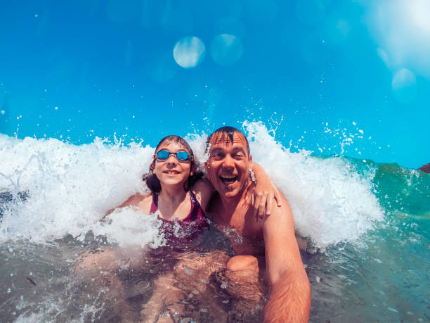 istock Father and daughter having fun on the waves splashing 1207839220