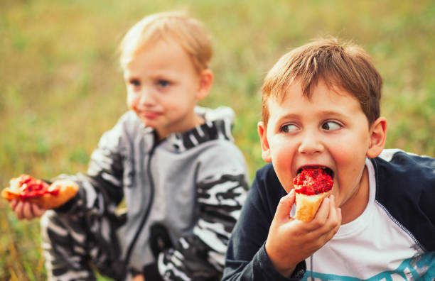 istock Two smiling boys with snacks on green grass 1207842919