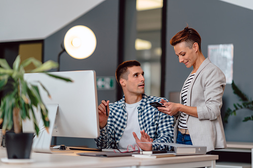 Businesswoman wearing casual clothes using smart phone and showing talking with colleague at the office while smiling