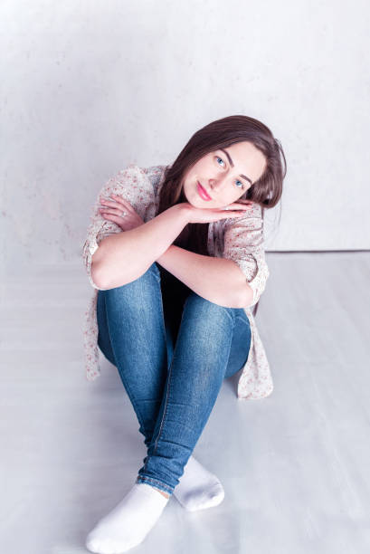 istock modest girl smiling and sitting on the floor 1207845847