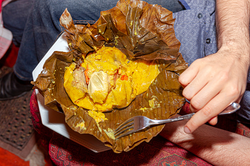 A Tamale that is ready to be eaten. A typical Colombian meal it is usually different types of meat, rice and egg, wrapped up in a banana leaf and steamed. The one on display will make a meal for one adult. Horizontal format.