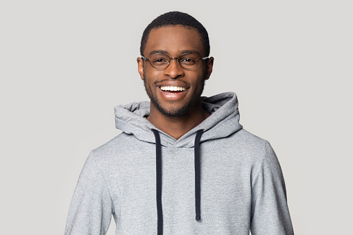 Joyful smiling millennial african american male student in stylish hoodie looking at camera head shot close up portrait. Laughing overjoyed happy black young man isolated on grey studio background.