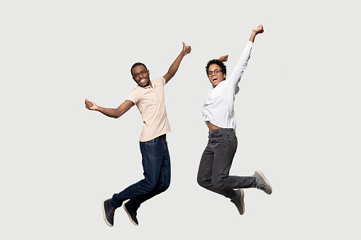 Full length crazy cheerful happy energetic euphoric african american couple friends jumping with raised hands, feeling overjoyed, having fun, playing together, isolated on grey studio background.