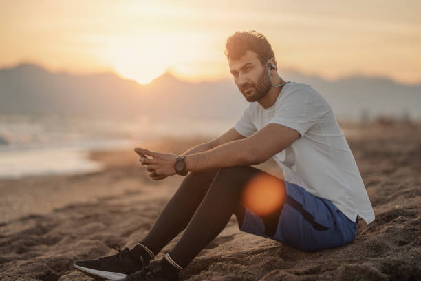 istock a man sitting on the beach with phone in hand 1207858300