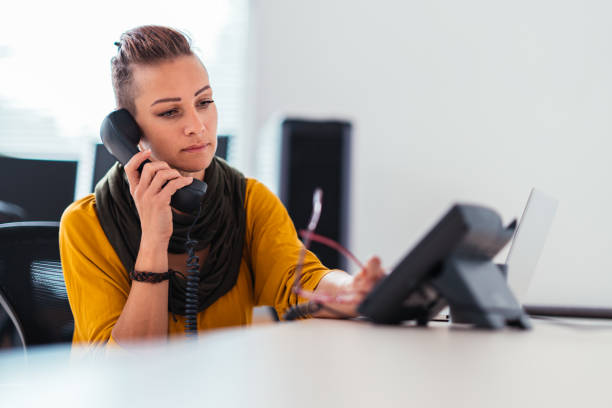 Businesswoman wearing yellow shirt using landline phone in the office