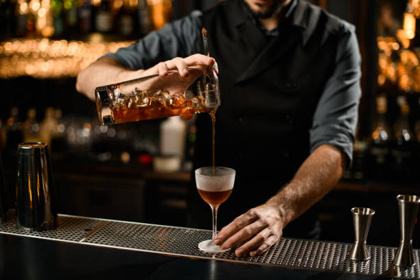 istock Professional bartender pouring a brown alcoholic cocktail drink from the glass through the strainer 1207862085
