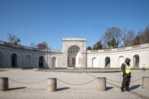 Arlington, VA, USA.  April 2, 2019.  A security person patrols one of the buildings at Arlington Cemetery in Virginia.  Another person seen walking in the background.