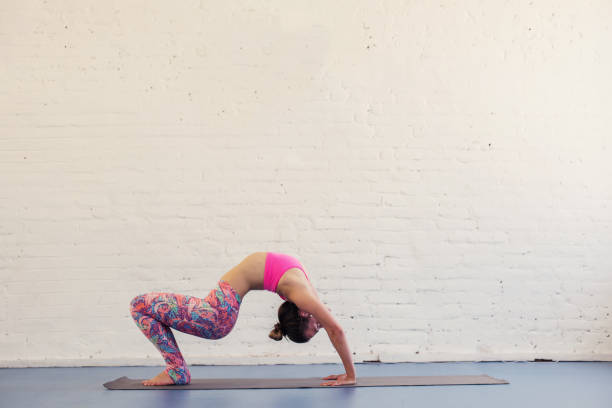 istock Flexible woman doing bridge  yoga exercise in studio. White brick wall on background 1207881421