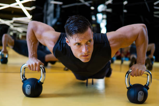 istock Muscular man in gym doing pushups exercise with kettle-bell in a workout. 1207887669