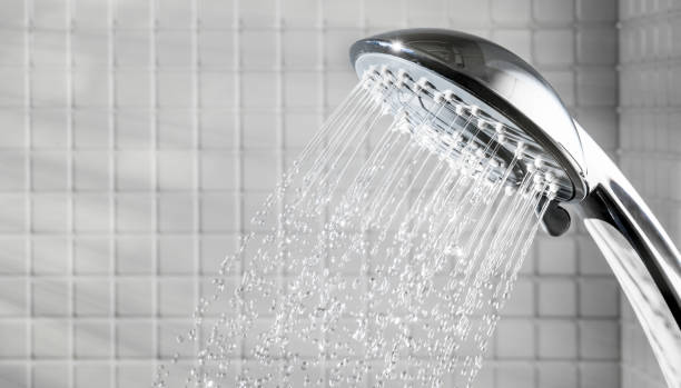 istock Shower head with running water in white bathroom 1207890735