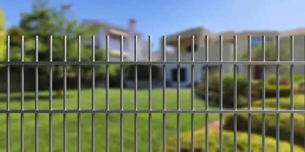 Photo of House safety. Metal fence with steel bars, blur residential building and garden background. 3d illustration