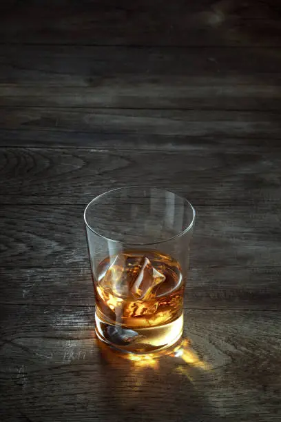 close up view of glass with ice and whiskey on wooden background