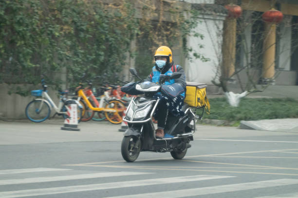 chinesischer liefermann trägt chirurgische maske liefert lebensmittel auf elektrofahrrad - senior women capsule senior adult medicine stock-fotos und bilder