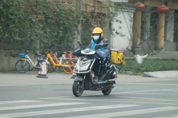 Chinese delivery man wearing surgical mask is delivering food on electric bike ChengDu China - Feb 22 2020: Since December 2019, Wuhan City, Hubei Province has found multiple cases of viral pneumonia, all of which were diagnosed with viral pneumonia / pulmonary infection.2019-nCoV coronavirus pneumonia in Wuhan has been spreading many cities in China.Chinese delivery man wearing surgical mask is delivering food on electric bike in ChengDu. chengdu photos stock pictures, royalty-free photos & images