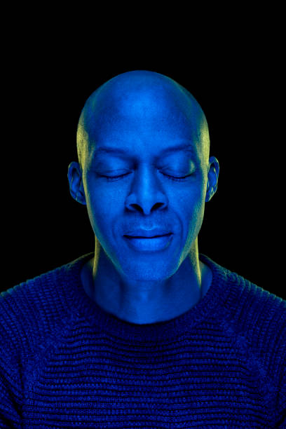 istock Black man with eyes closed. Studio photo with blue light isolated on black background. 1207922380