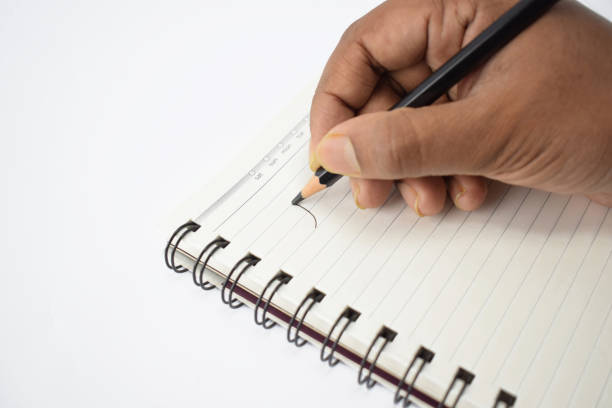 istock A person writing on a blank white notebook with a sharpened black pencil over a white background 1207924859