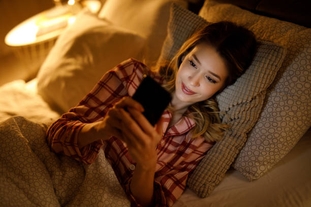 istock Beautiful young woman using mobile phone in bed 1207926392
