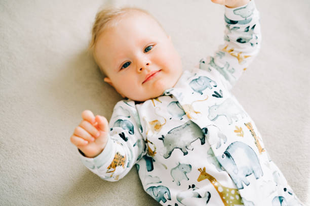 a small beautiful boy in a jumpsuit with animals is lying on the couch and looking at the camera a small beautiful boy in a jumpsuit with animals is lying on the couch baby boys stock pictures, royalty-free photos & images