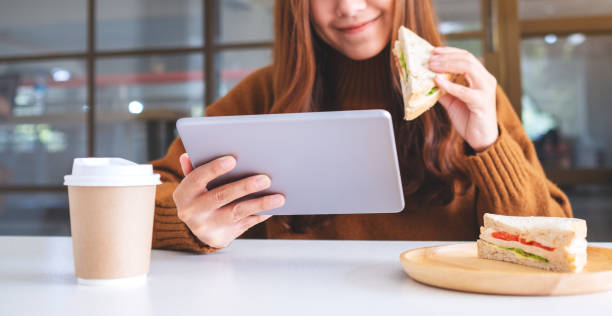 istock woman holding and eating whole wheat sandwich while using tablet pc 1207928178