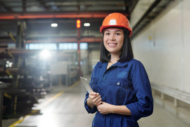 istock Pretty young smiling engineer in uniform and protective helmet holding tablet 1207928546
