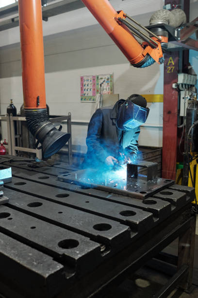 Professional welder in workwear and protective mask doing welding work Professional welder in workwear and protective mask welding parts of huge iron industrial machine in factory workshop Furnace stock pictures, royalty-free photos & images