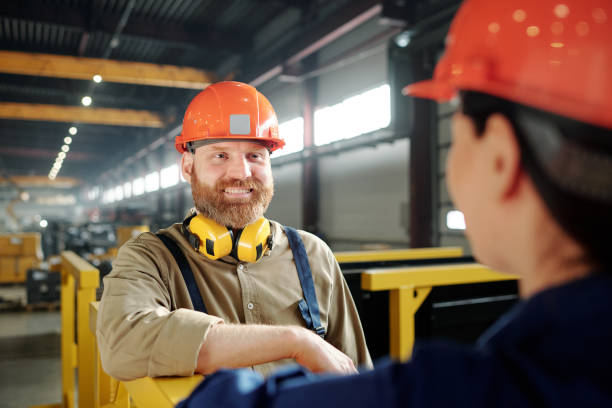 istock Happy young bearded engineer in hardhat talking to his colleague 1207928651