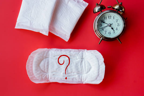 menstruation , concept de retard de période avec la serviette sanitaire avec le point d’interrogation sur le bloc-notes et le réveil sur le fond rouge - sanitary photos et images de collection
