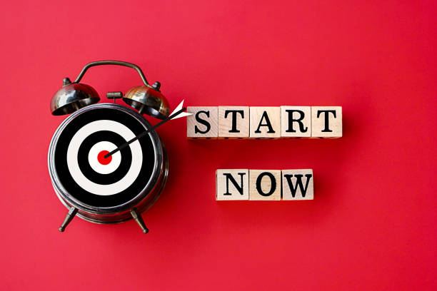 istock start now and target concept with text on wooden block and alarm clock on red background 1207935834