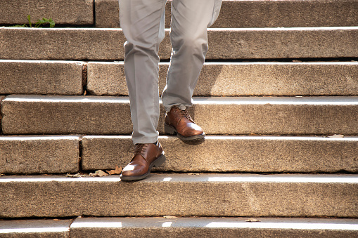 One men in brown shoes walking down the public outdoor stairway in autumn sunlight, detail of his legs in motion blur