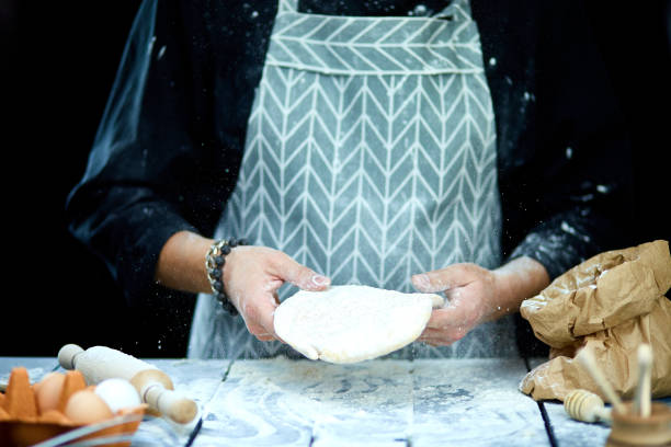 istock The man, chef cooks throws the dough, flying, freezing in motion. On a black background. White flour flying into air. Hands preparing dough 1207947993