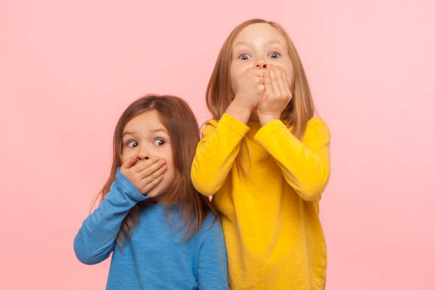 portrait of two little frightened girls covering mouth with hands and looking with scared eyes - segredo criança imagens e fotografias de stock