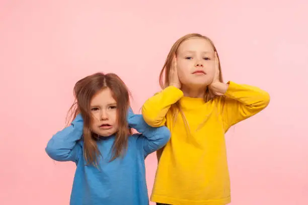 Photo of We don't want to listen! Portrait of two naughty disobedient little girls covering ears with hands, ignoring parental advice