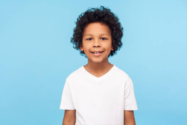 Portrait of cheerful little boy with curly hair in T-shirt smiling funny and carefree, showing two front teeth, healthy happy child Portrait of cheerful little boy with curly hair in T-shirt smiling funny and carefree, showing two front teeth, healthy happy child, positive emotions. indoor studio shot isolated on blue background 6 7 years stock pictures, royalty-free photos & images