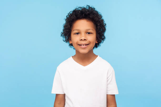 portrait of cheerful little boy with curly hair in t-shirt smiling funny and carefree, showing two front teeth, healthy happy child - six objects imagens e fotografias de stock