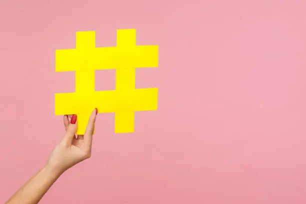 Photo of Closeup of hand holding large yellow paper hashtag symbol next to copy space, hash sign of famous media content