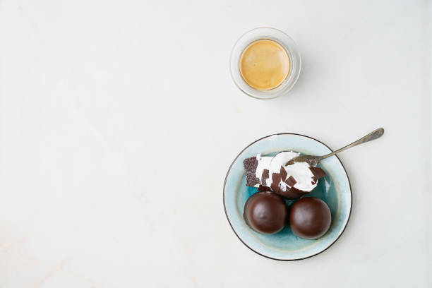 Whole and cracked Chocolate covered marshmallows, german "Schokokuss" or "Schokoschaumkuss" and glass of fragrant coffee over marble background. Top view. stock photo