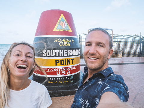 Cheerful couple taking selfie portrait with Southernmost point in Key West USA