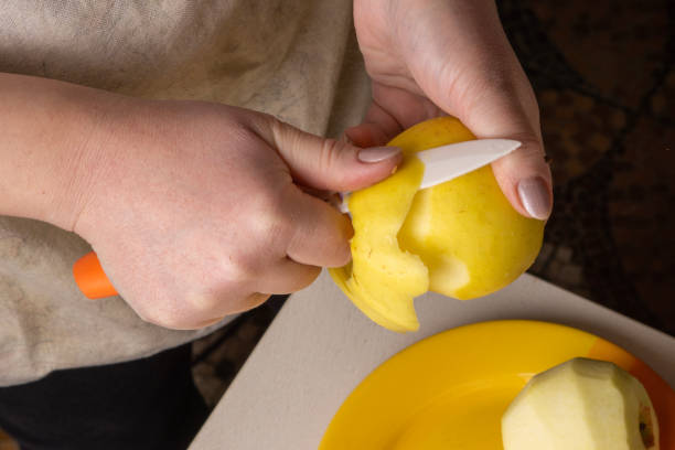 istock Hands of an elderly woman peeling an apple with a white ceramic knife. 1207968018