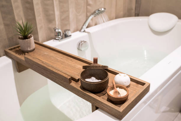 modern and comfortable bathroom, bath tub with wooden table and toiletries, salt, herb, bath bomb. - banho terapêutico imagens e fotografias de stock