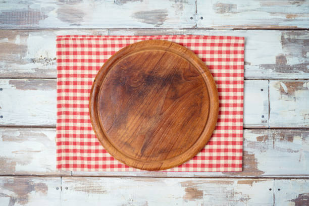 istock Round pizza board with red checked tablecloth on rustic wooden table .Kitchen, cooking or baking mock up background for design. 1207973705