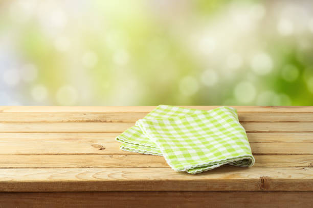 istock Empty wooden table with green checked tablecloth over green bokeh background. Spring and easter mock up for design. 1207973805