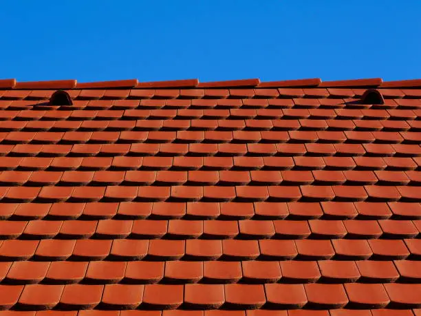 sloped red clay tile roof and ridge. clear blue sky in day light. construction, modern building materials and technology concept. abstract low angle view.