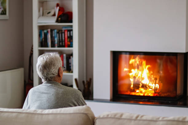 istock Old thoughtful gray haired man sitting on sofa in front of fireplace at home watching fire. Senior pensioner lifestyle. Loneliness. 1207984366