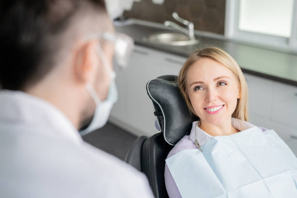 glückliche junge blonde patientin, die ihren zahnarzt mit gesundem lächeln anschaut - zahnarztstuhl stock-fotos und bilder