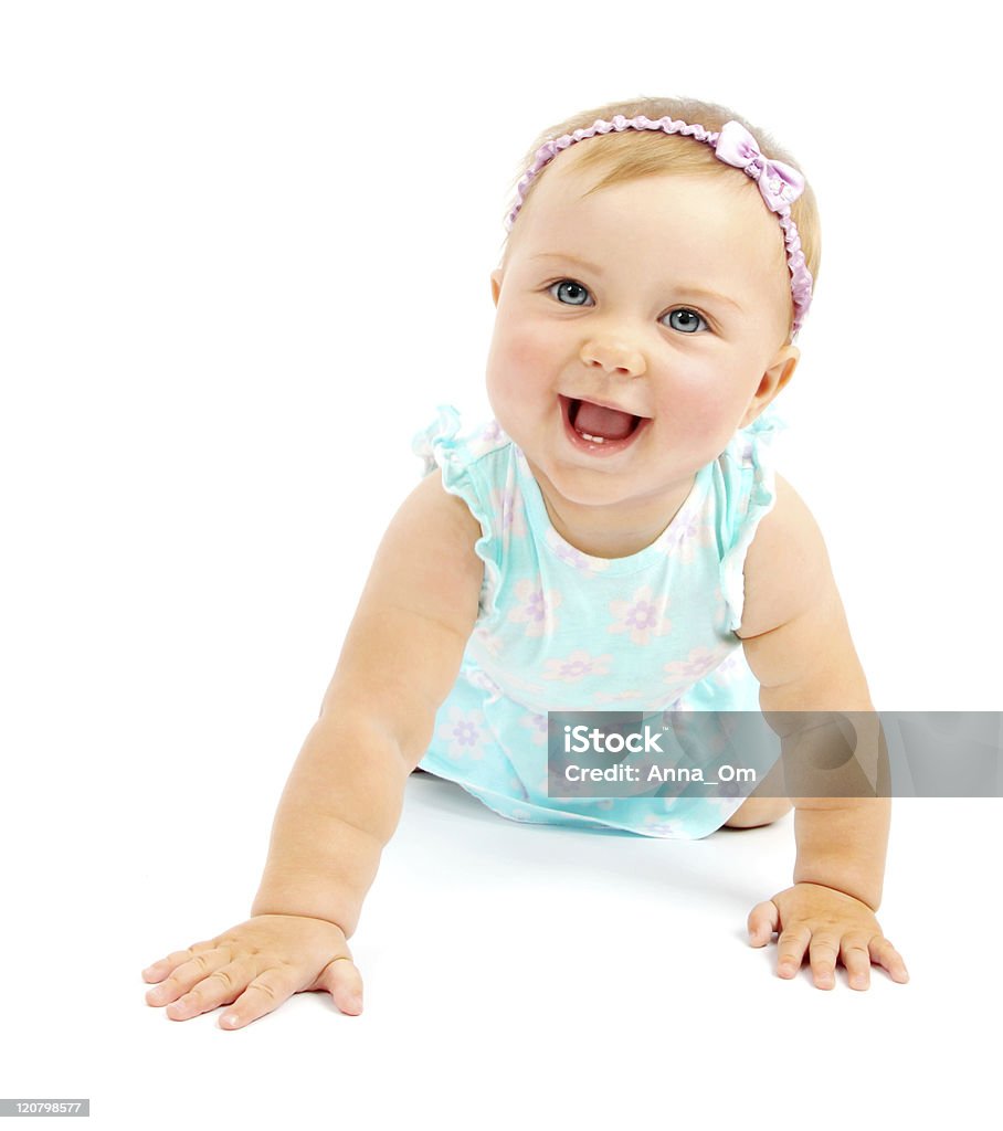 Blonde baby girl in blue dress holding herself up & smiling Adorable little baby girl laughing, creeping & playing in the studio, isolated on white background. Baby - Human Age Stock Photo