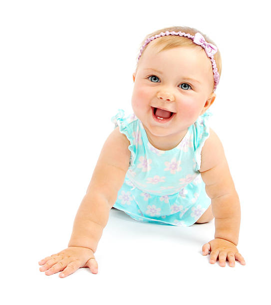Blonde baby girl in blue dress holding herself up & smiling stock photo
