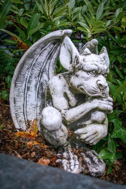 Garden decoration - a stone gargoyle figure sitting in a bed of green plants