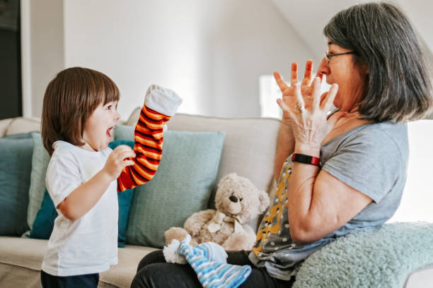 Cute little cheerful child playing with his older granmother with bright hand toy at home. Focus on boy. Family lifestyle. Active senior woman. Babysitting. stock photo