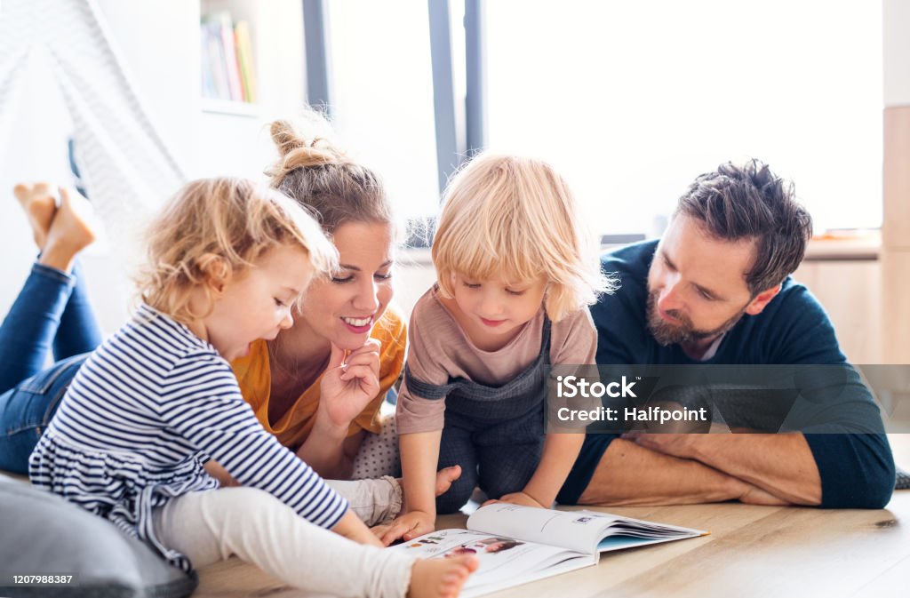 Junge Familie mit zwei kleinen Kindern drinnen im Schlafzimmer lesen ein Buch. - Lizenzfrei Familie Stock-Foto